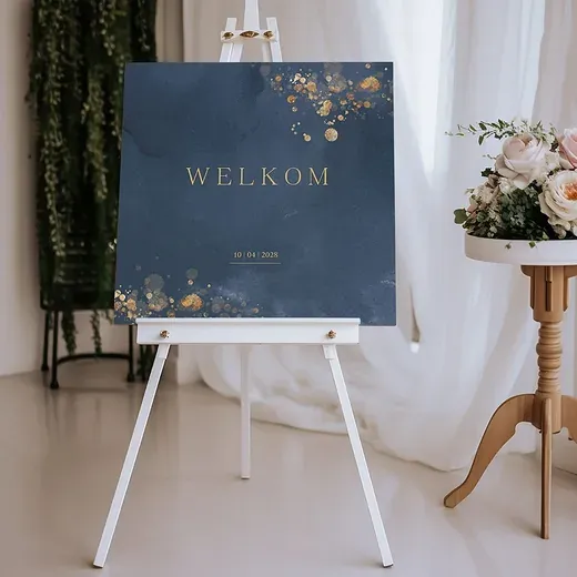 Donkerblauw welkomstbord met goudkleurige tekst Welkom op een witte schildersezel, naast een tafeltje met rozen